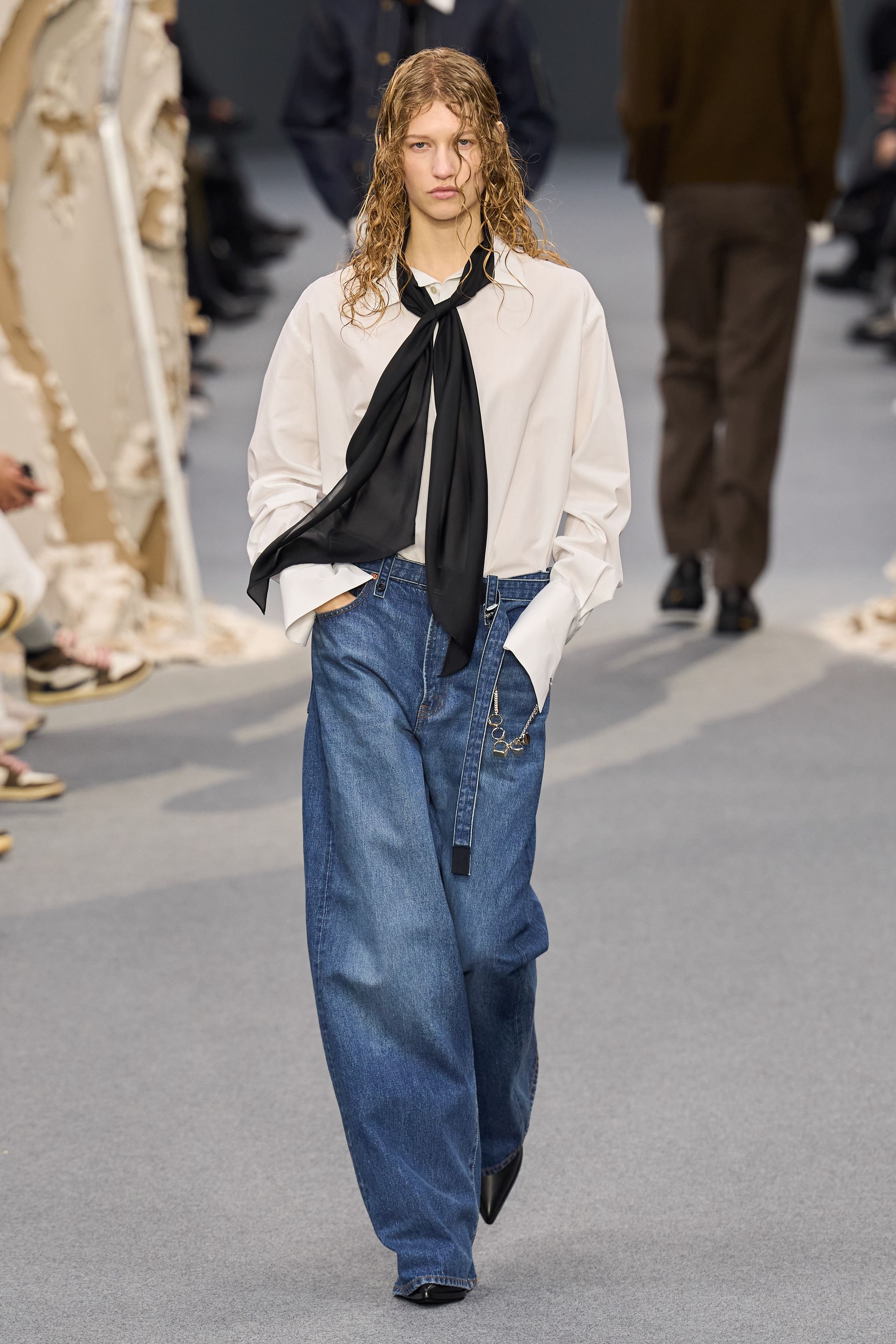 Sacai 2026秋冬再次展示其无可复制的“混合美学”。正装、牛仔、皮草与制服元素被高度结构化地拼接，形成既熟悉又陌生的服装形态。性别边界被进一步模糊，层叠结构制造流动节奏，使行走本身成为设计的一部分。系列在秩序与混乱之间找到平衡，是Sacai 对当代复杂生活状态的持续回应-顽石频道趋势研究